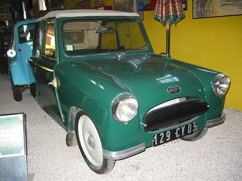 Green small two-seat coupé with a cream roof and white-wall tyres in a museum. Opens a larger view