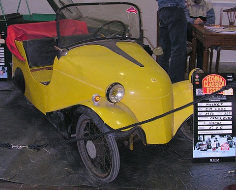 Yellow open two-seater with black wings behind a rope, an information board beside it. Opens a larger view