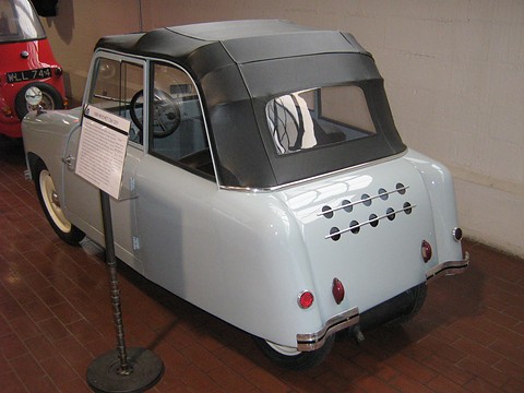 Rear of a pale blue small coupé with a black fabric top and two rows of round vents. Opens a larger view