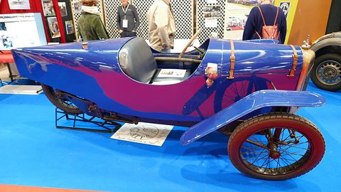 Side view of a long, pointed blue single-track car with leather straps on the bonnet and a cycle wing over the front wheel. Opens a larger view