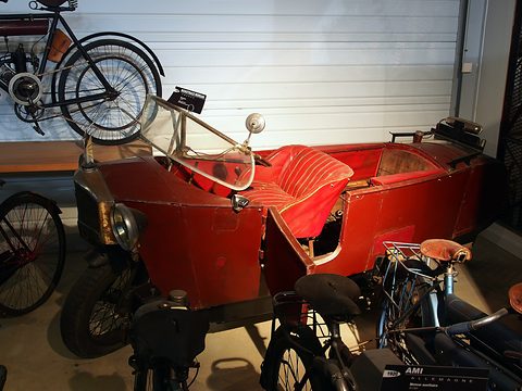 A red narrow open car with red upholstered seats and an open side door, bicycles hanging on the wall above. Opens a larger view