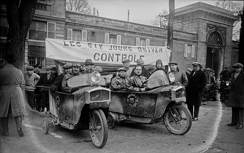Two mud-spattered narrow single-track cars with crews in leather coats in front of a banner reading Les Six Jours d’Hiver Contrôle. Opens a larger view