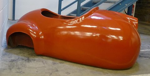 Glossy orange moulded body shell with no wheels or fittings, lying on a concrete floor by a stair. Opens a larger view