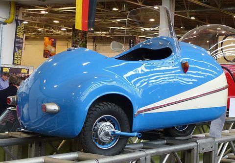 Blue and cream single-seat replica on a steel display rack in an exhibition hall. Opens a larger view