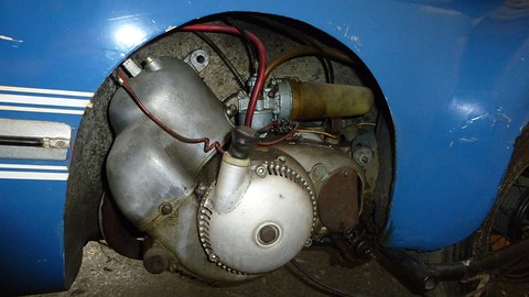 Close view of a small finned aluminium engine with wiring, set into a cut-out in blue bodywork. Opens a larger view