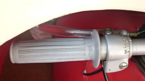 Ribbed grey handlebar grip with a Magura control and brake lever, red seat behind. Opens a larger view