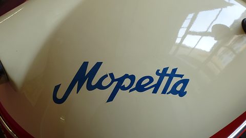 Blue painted Mopetta lettering on glossy cream bodywork, a window reflected above. Opens a larger view
