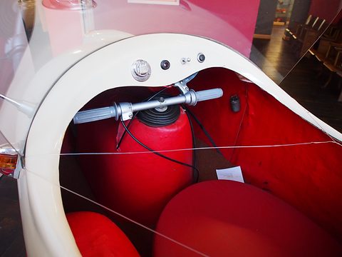 Looking into a cream single-seater: handlebar on a red fuel tank and a red seat, a display wire across.