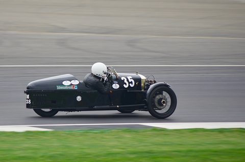 A black streamlined three-wheeler numbered 35 with a helmeted driver on a track, grass verge in the foreground. Opens a larger view
