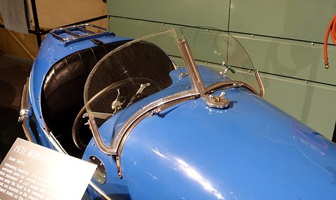 A curved glass windscreen in a chrome frame on blue bodywork, a filler cap in front, black seat behind. Opens a larger view