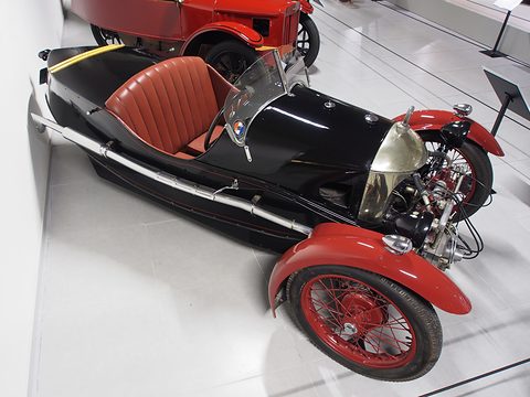 Looking down on a black three-wheeler with red leather seats, red wings and a polished cowl. Opens a larger view