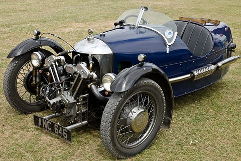 A dark blue beetle-backed three-wheeler with a polished cowl and exposed JAP engine parked on grass. Opens a larger view