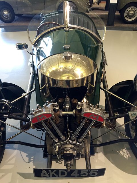 Front view of a three-wheeler: a polished domed cowl above a V-twin with red M badges and the plate AKD 455. Opens a larger view