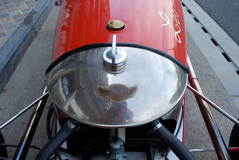 Close view from above of a polished domed cowl with a winged badge and a filler cap on red bodywork. Opens a larger view