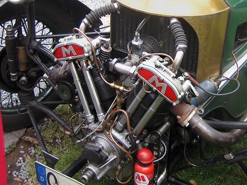 Close view of an air-cooled V-twin with red Matchless badges, copper pipes and a red oil bottle, grass below. Opens a larger view