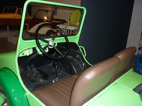 Green open car interior with a black three-spoke wheel, a bare floor and a brown leather bench seat. Opens a larger view