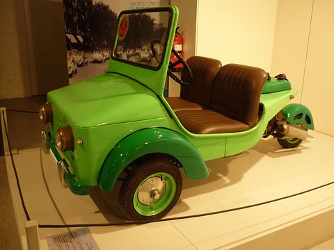 Bright green open three-wheeler with a brown leather bench seat, a tall windscreen and a single rear wheel.