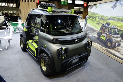 Khaki and lime-green open two-seater with a roof light bar, spare wheel and off-road tyres on a show stand.