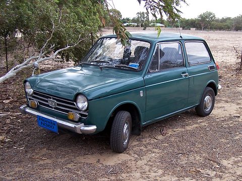 Dark green small saloon with a blue plate parked on dusty ground under eucalyptus trees. Opens a larger view