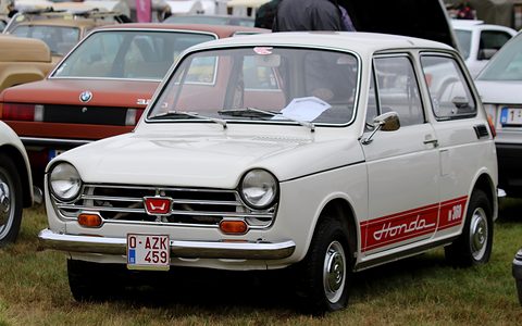White small saloon with a red side stripe and a Belgian plate, on grass among old cars. Opens a larger view