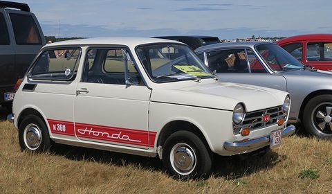 White small saloon with a red stripe lettered Honda along the sill, parked on grass. Opens a larger view