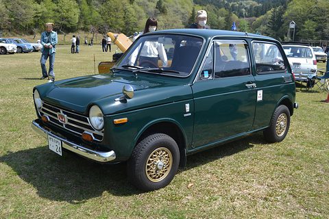 Dark green small saloon with gold alloy wheels on grass, visitors behind. Opens a larger view