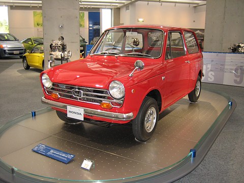 Red small two-box saloon on a round display platform in a bright hall with pillars. Opens a larger view