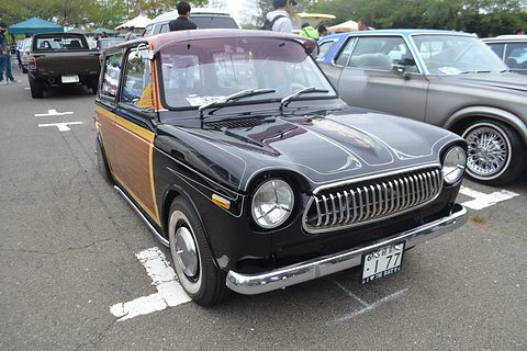 Black small estate van with wood-effect panels and a chrome vertical-bar grille in a car park. Opens a larger view
