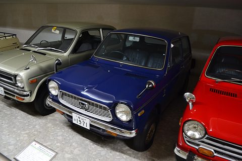 Navy small saloon between a pale car and a red car in a museum row. Opens a larger view