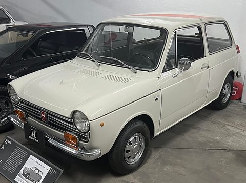White small saloon on a grey floor beside a placard, a dark car behind.