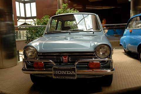 Pale blue small saloon with a HONDA plate on a tiled floor in a dim hall. Opens a larger view