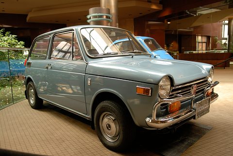 Pale blue small saloon on a tiled floor with a blue bubble car behind. Opens a larger view