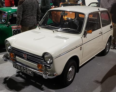 White small saloon on a grey show floor, visitors standing behind. Opens a larger view