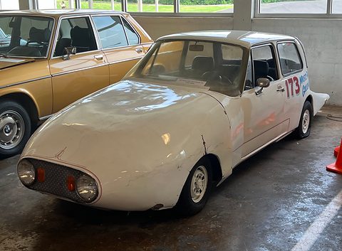 White small car with a long smooth faired nose and a number 173, in a museum. Opens a larger view