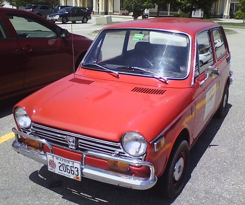 Red small saloon with a Maine plate parked on tarmac, other cars behind. Opens a larger view