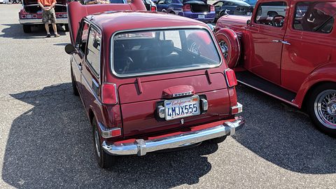 Rear three-quarter of a dark red small saloon with a California plate, a red pickup beside it. Opens a larger view