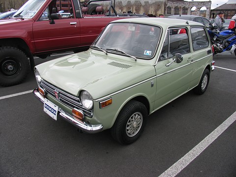 Pale sage-green small saloon in a car park beside a red pickup. Opens a larger view