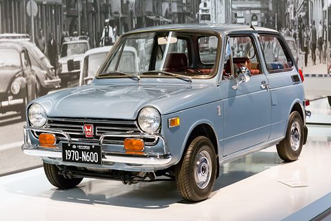 Pale blue small saloon on a white plinth with a 1970-N600 museum plate, an old photograph behind. Opens a larger view