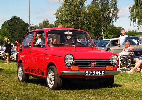 Red small saloon with black Honda lettering on its flank, on grass with visitors around. Opens a larger view