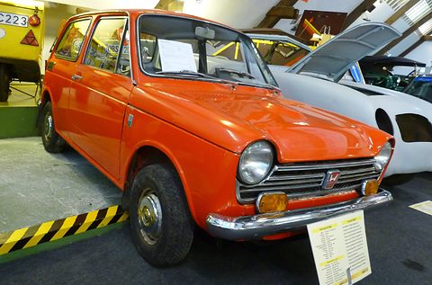 Orange small saloon with a placard on a stand, other cars crowded around it. Opens a larger view