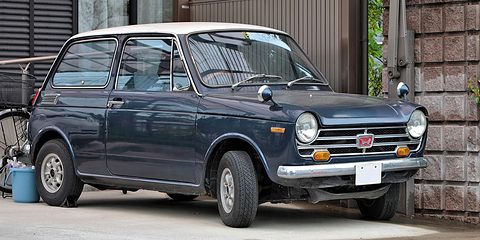 Dark navy small saloon with a white roof and chrome grille, parked beside a stone wall. Opens a larger view