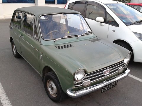 Olive green small saloon with a dull finish parked beside a white people carrier. Opens a larger view