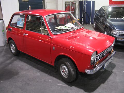 Red small saloon with a brochure on its dashboard in a hall with display stands. Opens a larger view