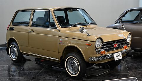 Gold small saloon with whitewall tyres and a HONDA N360 plate on a dark tiled floor.