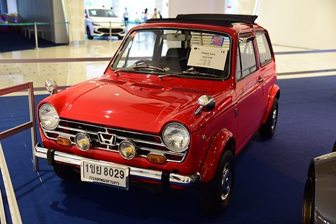 Red small saloon with fog lamps and a Thai plate on a blue carpet in a mall. Opens a larger view