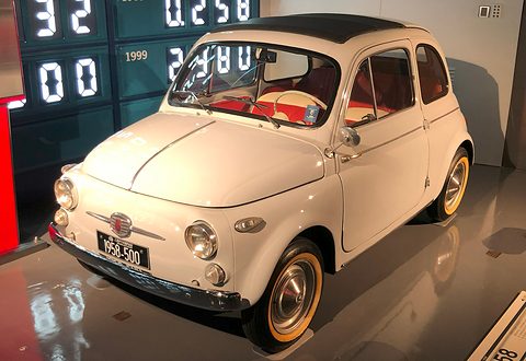 Cream Fiat 500 with cream-rimmed wheels and a black plate reading 1958-500, before a glowing digital counter wall. Opens a larger view