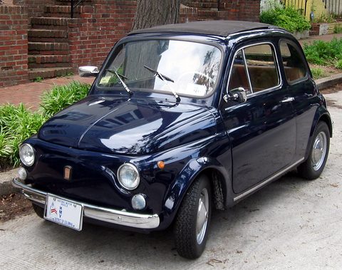 Navy Fiat 500 parked on a pavement beside brick steps and shrubs, its fabric roof closed. Opens a larger view