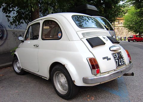 White Fiat 500 from the rear right with black louvre covers and a black Italian plate, by a graffiti wall. Opens a larger view