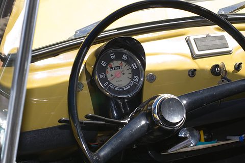 Yellow painted dashboard with a round speedometer, a thin black steering wheel and a few switches. Opens a larger view