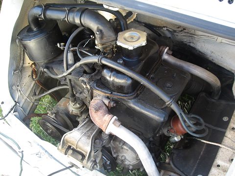 Close view into an engine bay with a black air-cooled twin, a cooling fan housing and an oil filler cap. Opens a larger view